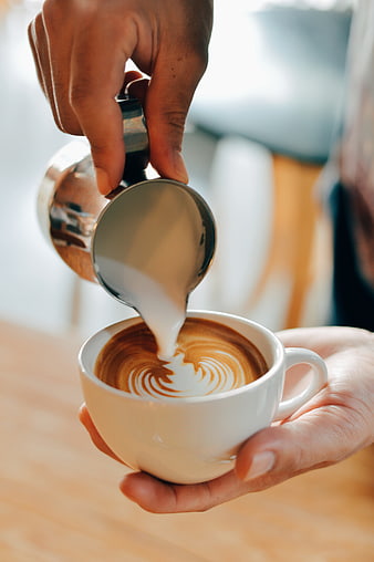 Barista pouring steamed milk into coffee cup for latte art