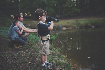 Young boy fishing by lake with father and brother