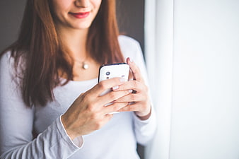 Woman holding white smartphone near window
