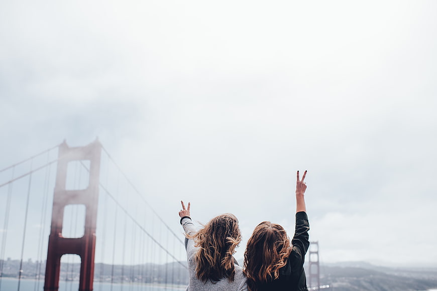 Two women making peace signs with Golden Gate Bridge background