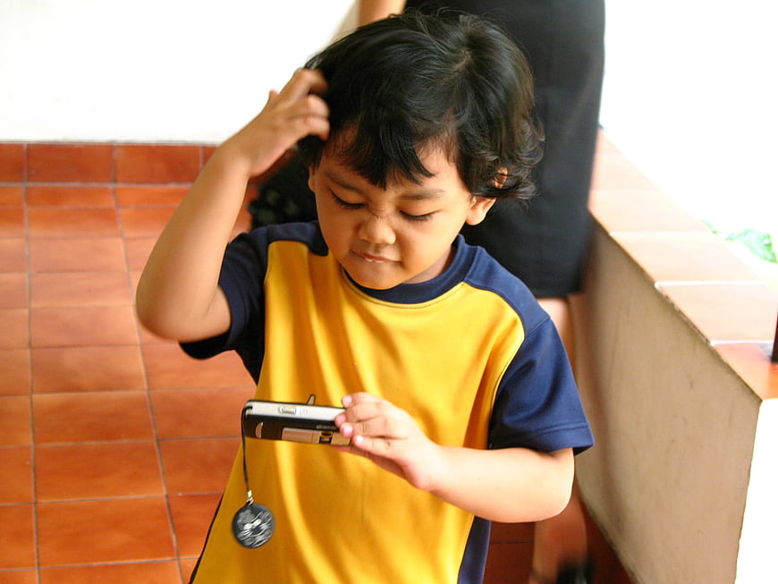 Young Boy Scratching Head While Looking at Mobile Phone