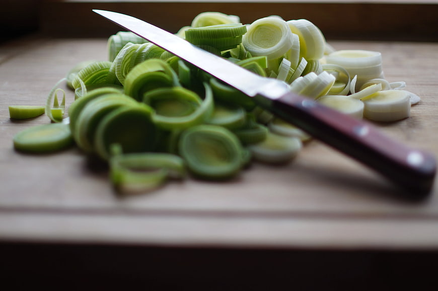 Sliced leeks and knife on wooden cutting board