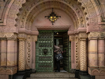 Man entering ornate stone archway with green metal doors