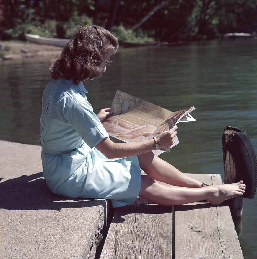 Vintage photo of woman reading magazine on wooden dock by lake