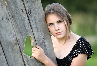 Young woman leaning against rustic wooden fence with heart cutout