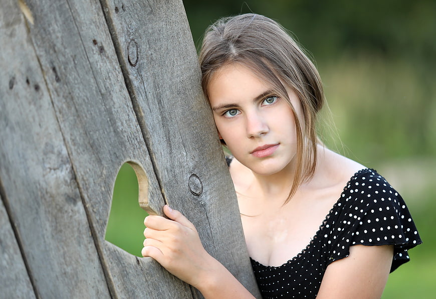 Young woman leaning against rustic wooden fence with heart cutout