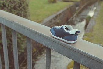 Blue baby sneaker on metal railing by stream