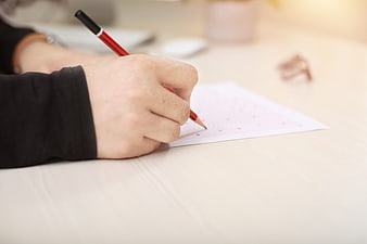 Close-up of hand filling out an exam paper with a red pencil