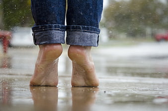 Bare feet in rain puddle wearing rolled up jeans