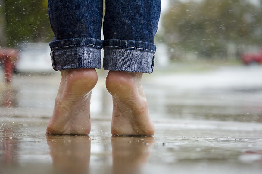 Bare feet in rain puddle wearing rolled up jeans
