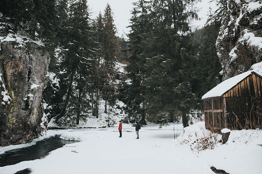 Couple standing on frozen river in snowy mountain forest