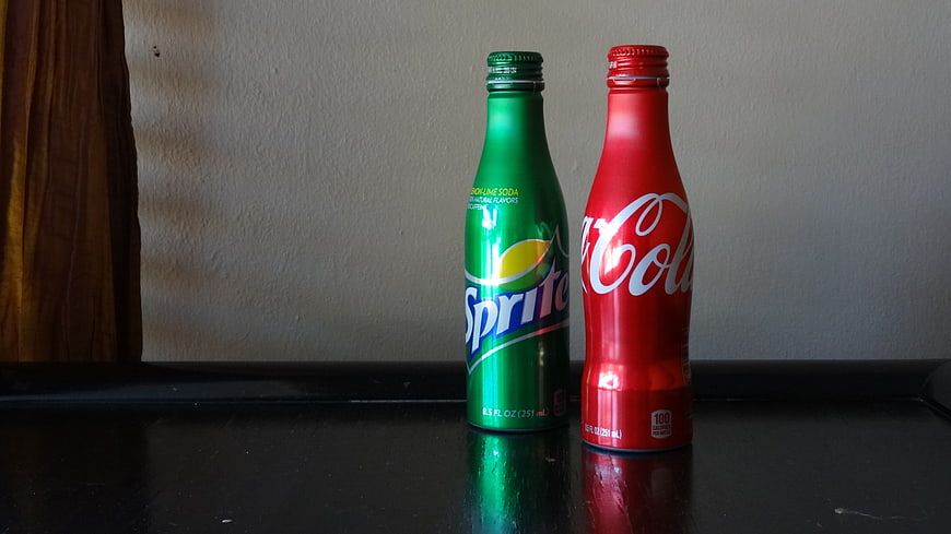 Sprite and Coca-Cola Aluminum Bottles on Dark Surface