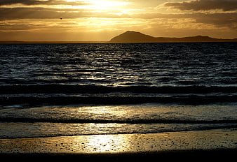 Golden Sunset Over Ocean Waves and Distant Island Silhouette