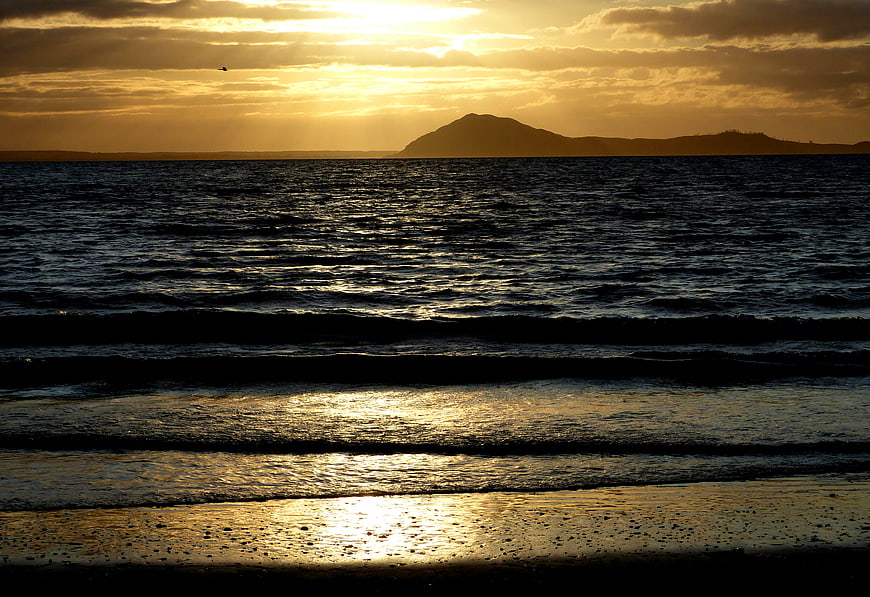 Golden Sunset Over Ocean Waves and Distant Island Silhouette