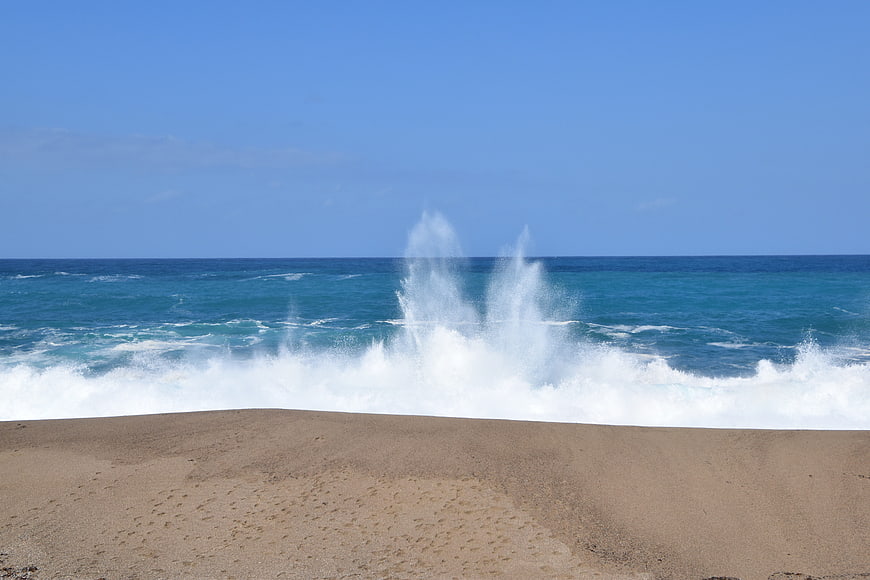 Powerful ocean waves crashing on sandy beach under blue sky