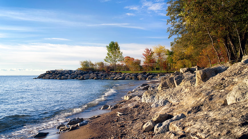 Rocky Lake Shoreline with Autumn Trees and Blue Sky