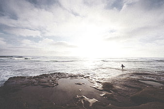 Lone Surfer Standing in Shallow Ocean Water on Rocky Shore