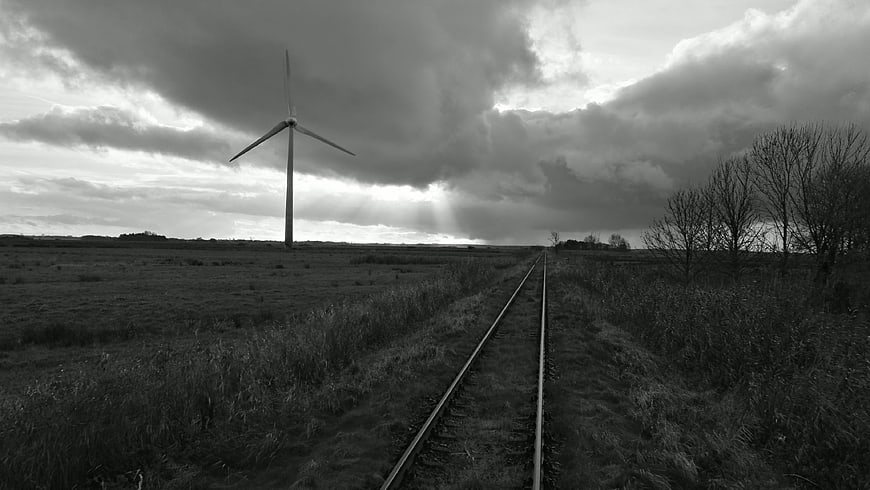 Black and white wind turbine and railroad tracks in field