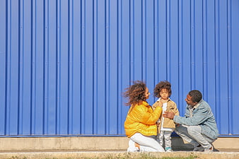 Family of Three Crouching in Front of Blue Wall
