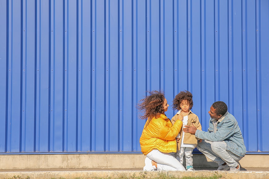Family of Three Crouching in Front of Blue Wall
