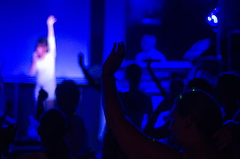 Woman singing on stage with raised hand in blue light