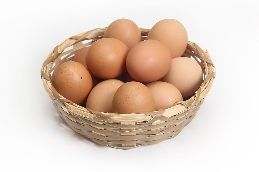 Fresh Brown Eggs in Woven Basket on White Background