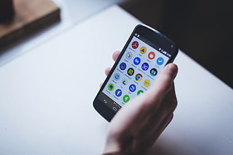 Hand holding smartphone with app icons on white desk