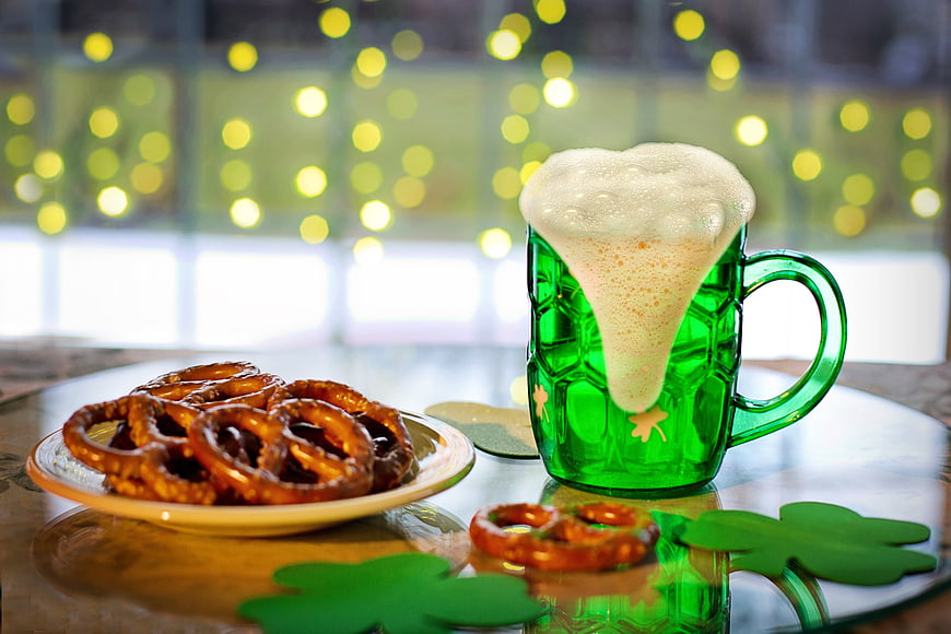 Green Shamrock Beer Mug With Pretzels And Coasters On Table