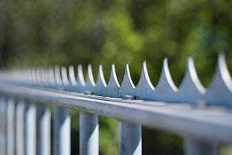 Close-up of metal fence spikes with blurred green background