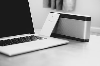 Black and white workspace with laptop, smartphone, and speaker