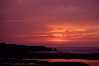 Vibrant Pink and Orange Sunset Over Silhouetted Coastal Cliffs