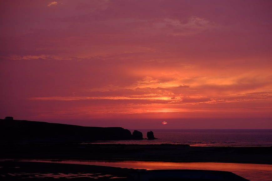 Vibrant Pink and Orange Sunset Over Silhouetted Coastal Cliffs