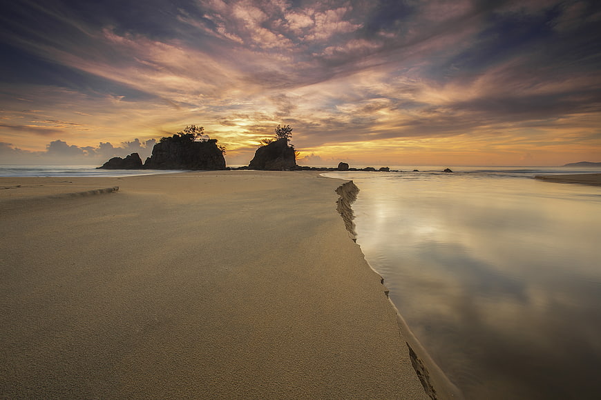 Serene Sunset Beach with Silhouetted Rock Formations