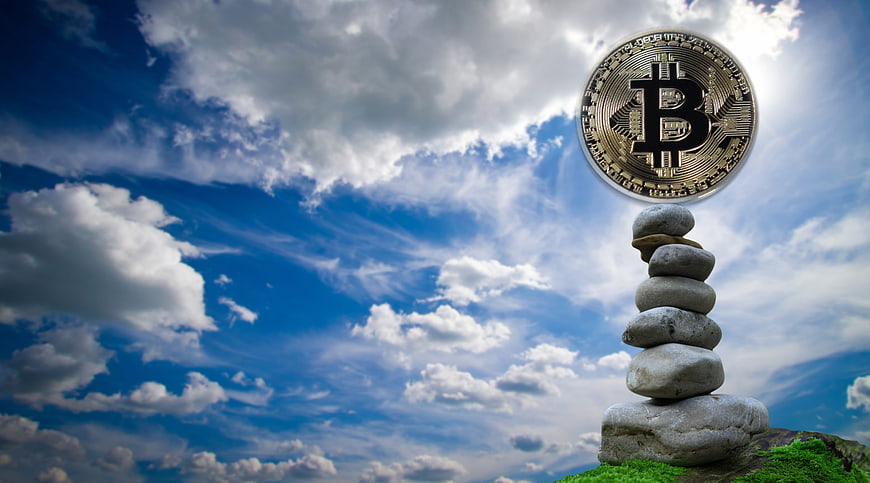 Bitcoin coin balanced on stacked stones against blue sky