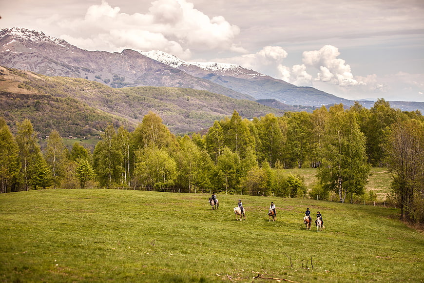 Group of Horse Riders in Green Meadow with Mountains