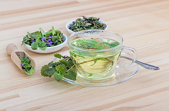 Fresh herbal tea with green leaves in glass cup on wood