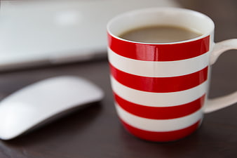 Red and white striped coffee mug on a dark desk with a computer mouse