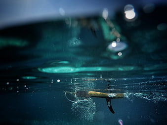 Underwater view of surfboard fin and bubbles in ocean