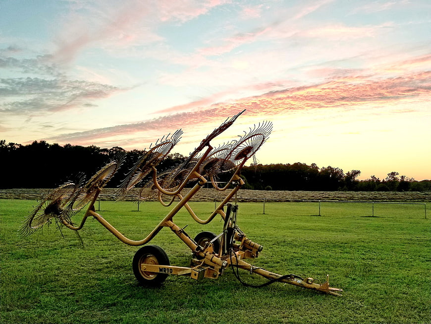 Vintage hay rake in green field at sunset
