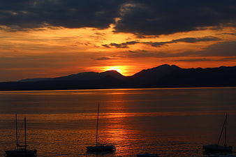 Dramatic Sunset Over Lake Garda With Silhouetted Sailboats And Mountains