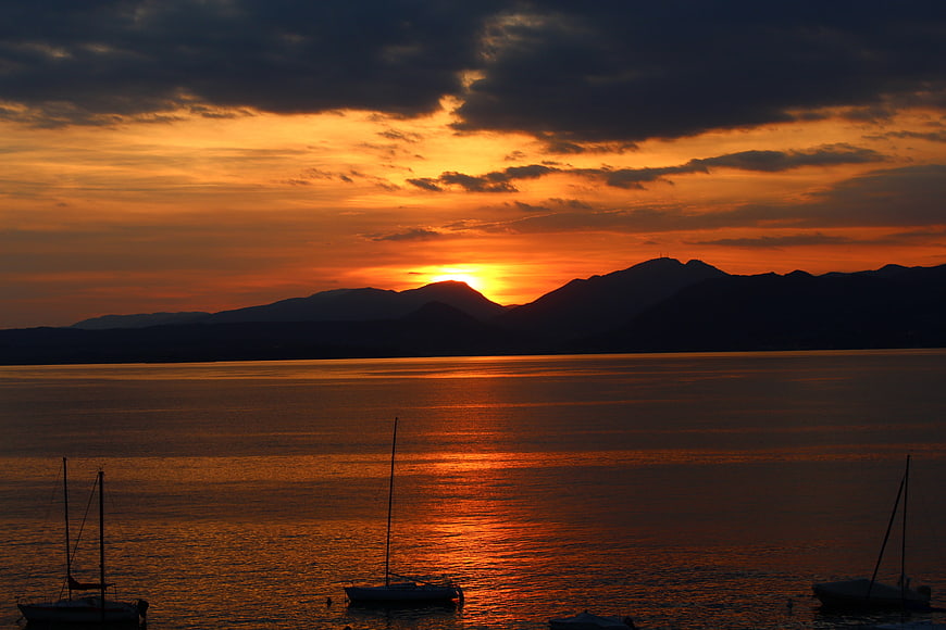 Dramatic Sunset Over Lake Garda With Silhouetted Sailboats And Mountains