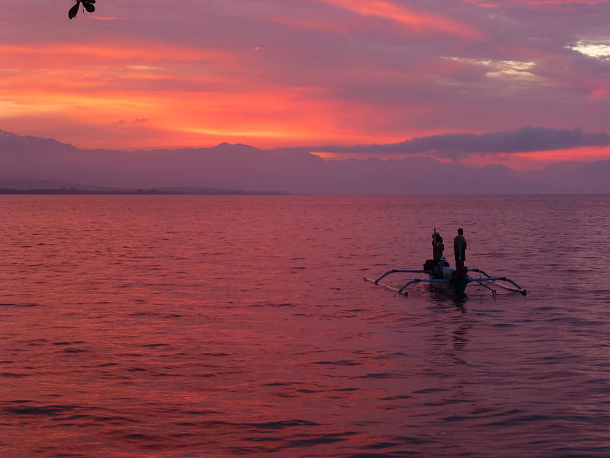 Silhouette of fishermen on outrigger boat at sunset
