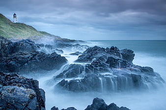 Dramatic Lighthouse on Rocky Coast with Misty Ocean Waves