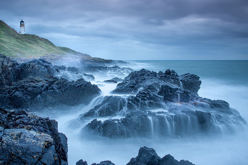 Dramatic Lighthouse on Rocky Coast with Misty Ocean Waves