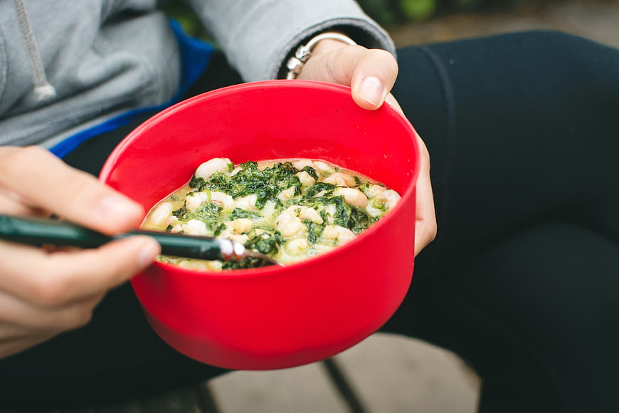 Close-up of hands holding red bowl with shrimp and spinach soup