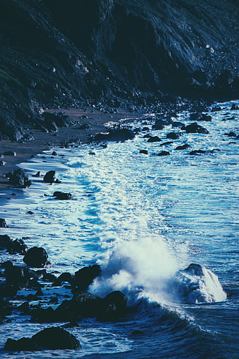 Dramatic blue ocean waves crashing on rocky shore
