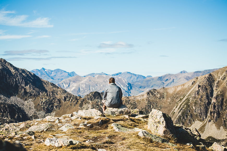 Man sitting on mountain peak overlooking vast valley landscape