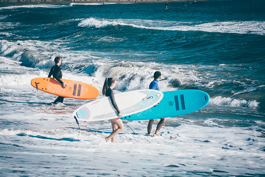 Surfers walking into ocean waves with colorful surfboards