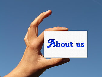 Hand holding white card with blue About us text against blue sky
