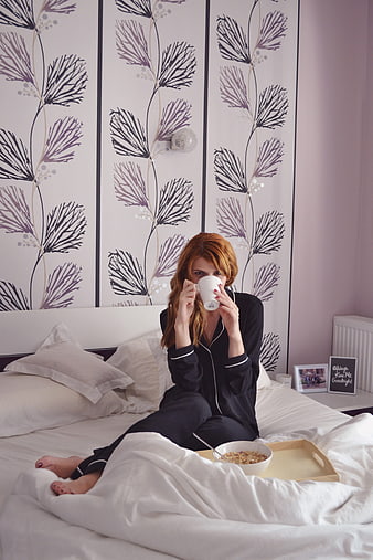 Woman in black pajamas enjoying breakfast in bed with coffee and cereal